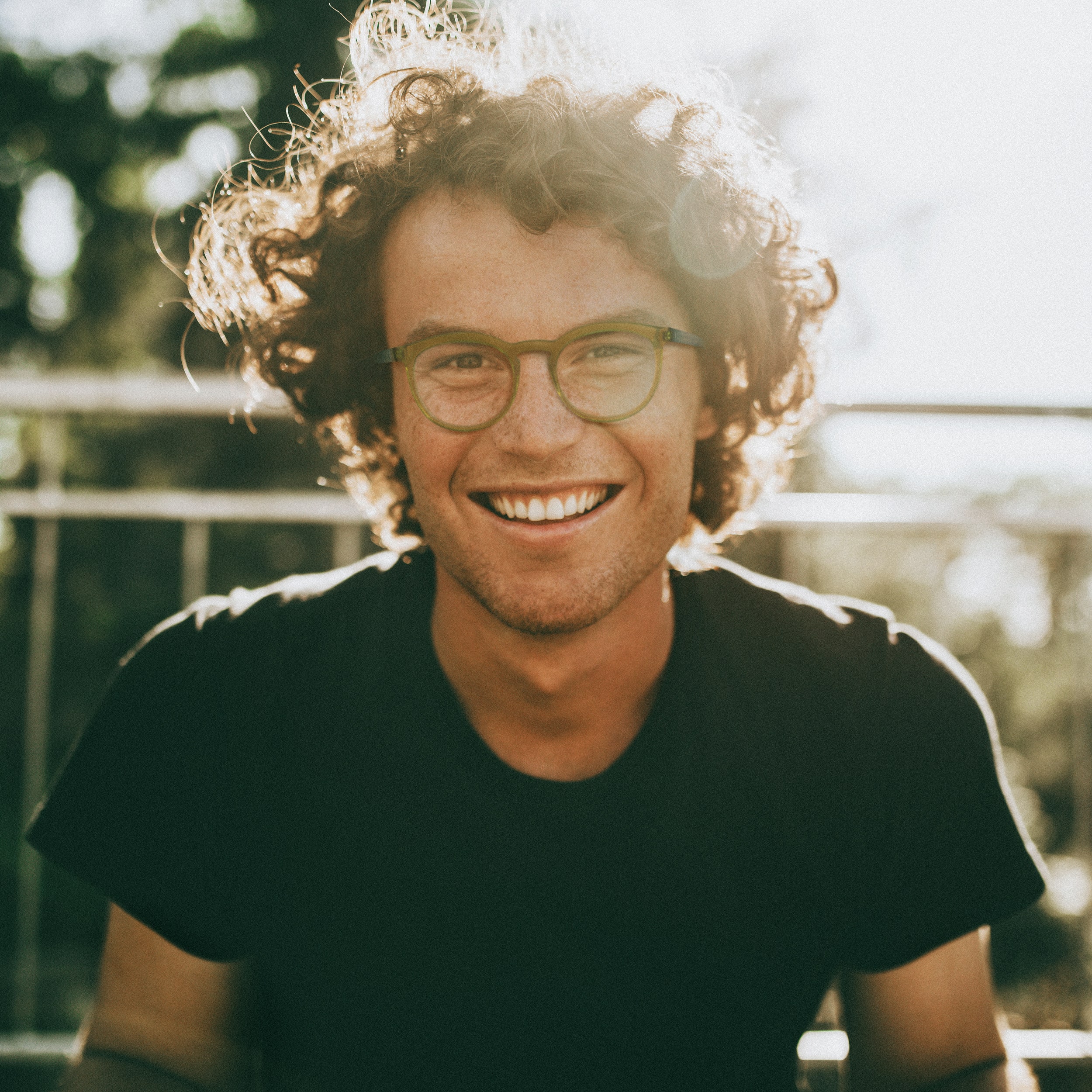 Homme souriant cheveux frisés porte des lunettes plastiques kaki