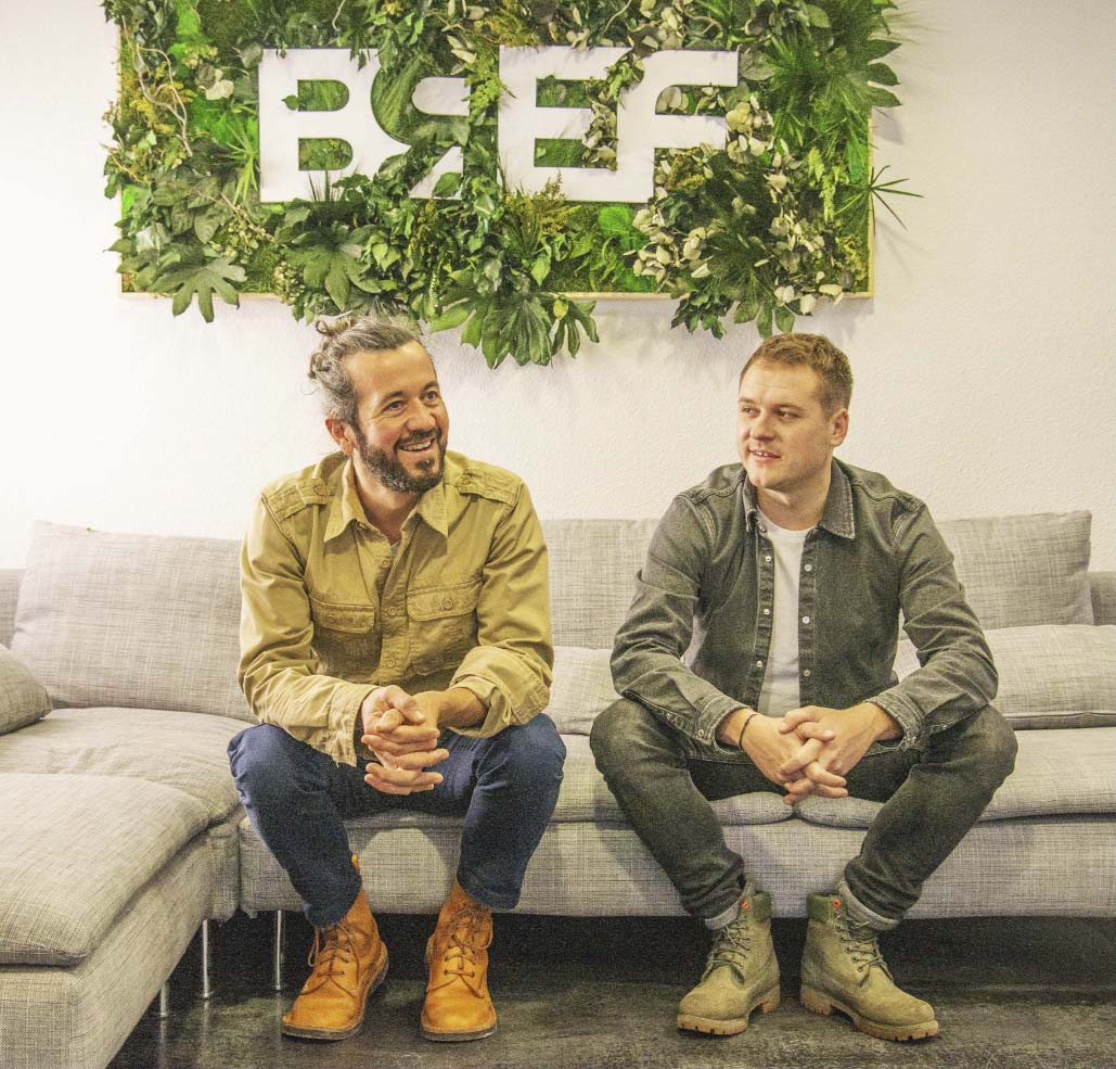 Ghislain et Léo, créateurs de la marque BREF, souriants, assis sur canapé